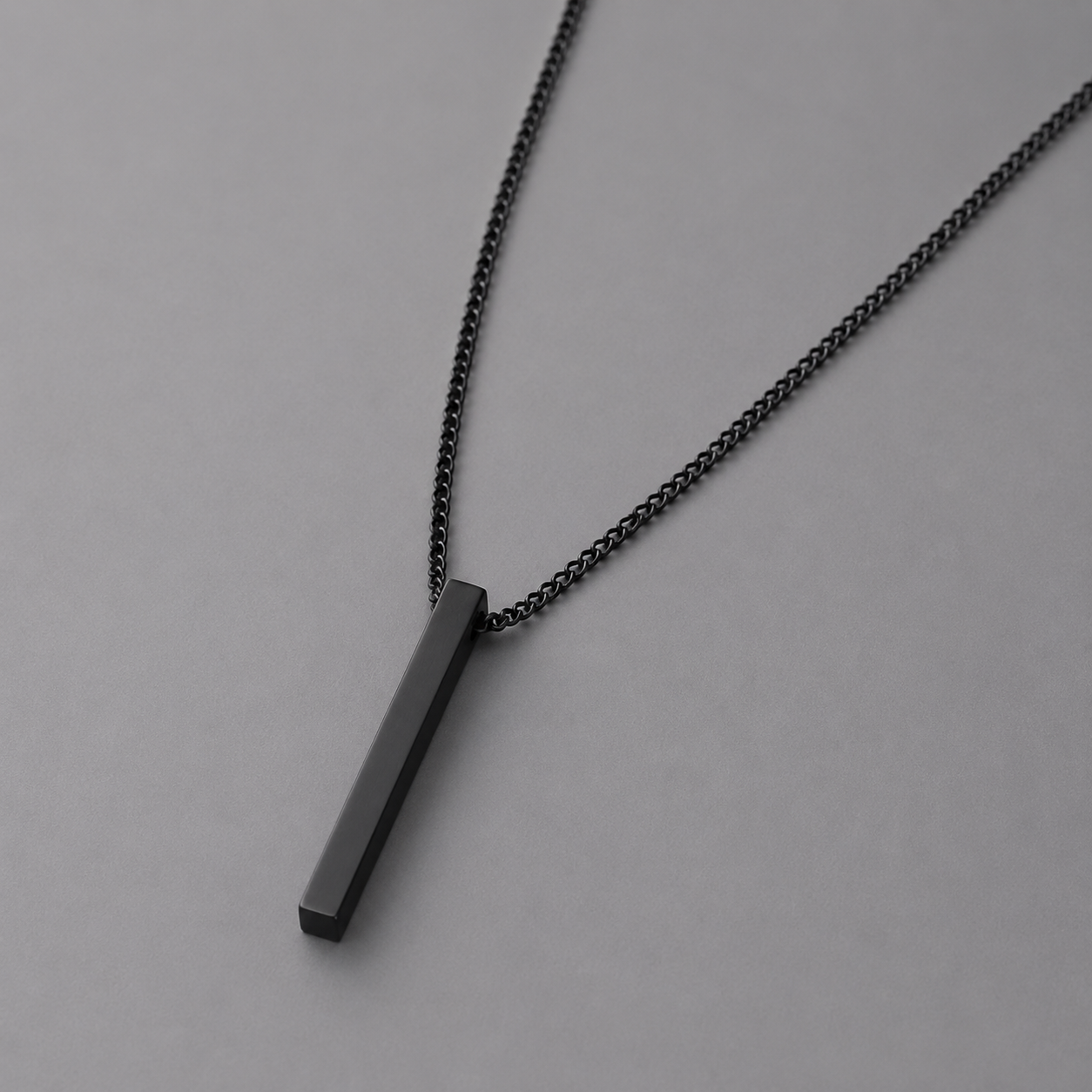 Black necklace with a rectangular pendant on a grey background