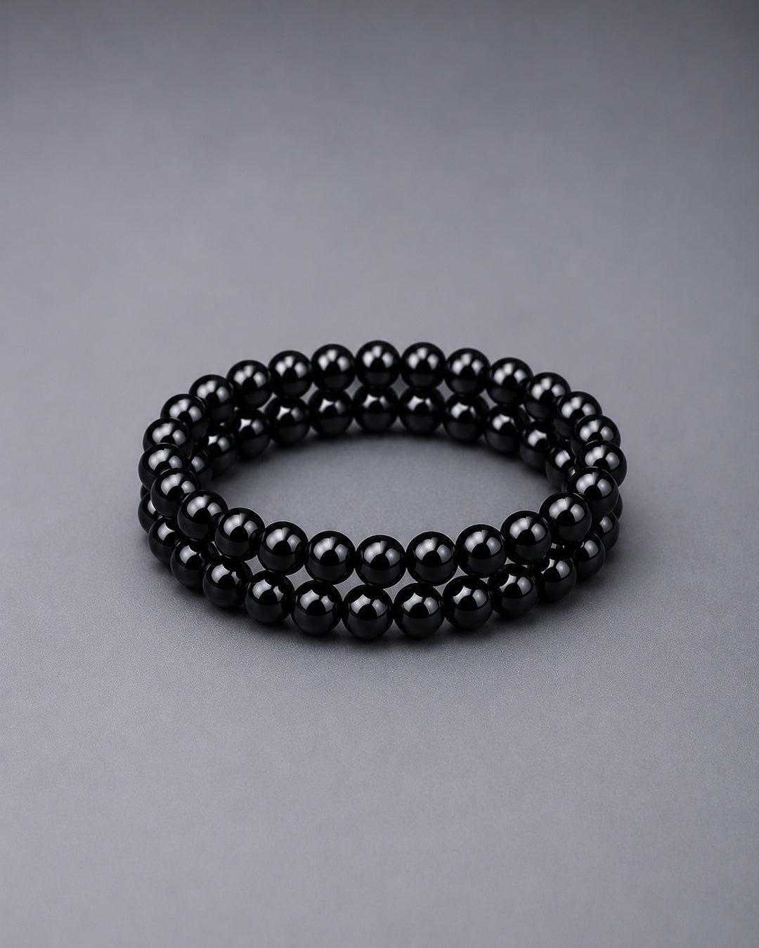 Black beaded bracelets on top of each other on a grey background