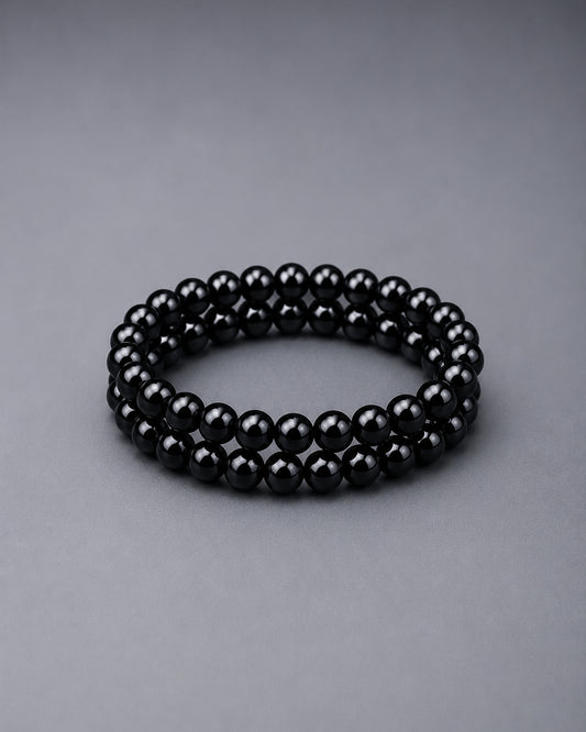 Black beaded bracelets on top of each other on a grey background